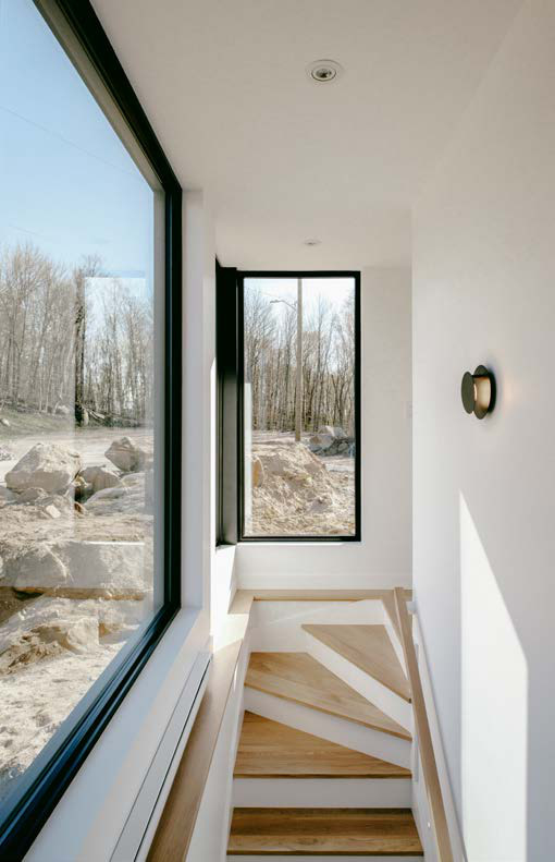 Grande fenêtre fixe noire éclairant une cage d'escalier en bois