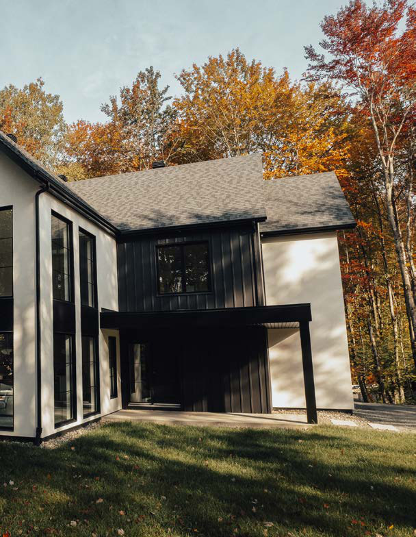 Maison blanche et noire aux grandes fenêtres noires, entourée d'arbres d'automne
