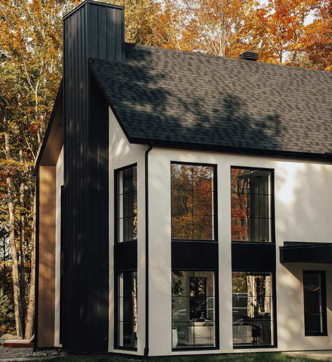 Maison blanche et noire aux grandes fenêtres noires, entourée d'arbres d'automne