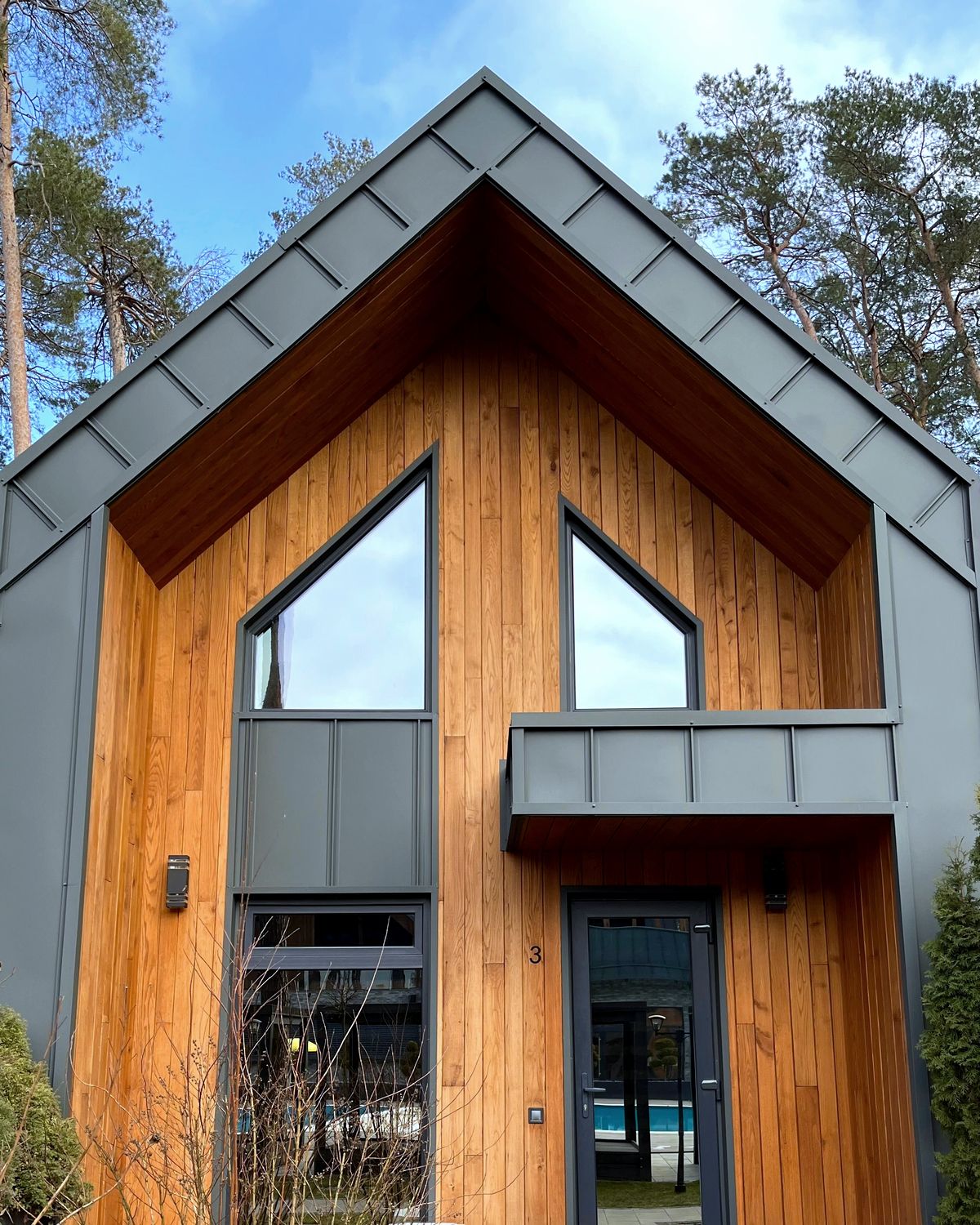 Maison contemporaine à pignon revêtue de bois, fenêtres triangulaires sous le toit